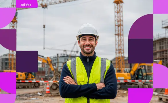 Engenheiro civil sorrindo de braços cruzados em um canteiro de obras. Ele usa capacete branco e colete reflexivo amarelo. Ao fundo, guindastes e tratores em uma construção desfocada, com grafismos roxos da marca Sólides nas laterais.