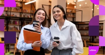 Duas profissionais conversando sorridentes em um escritório, ilustrando a diferença entre os cargos de auxiliar, assistente e analista.